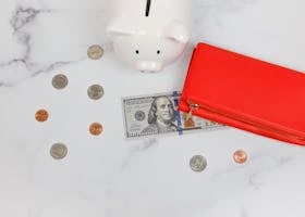Overhead view of piggy bank, red wallet, and US dollars on marble surface.